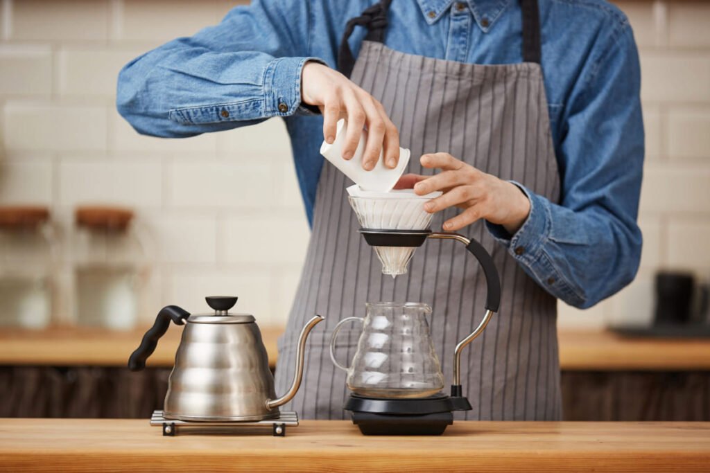What Is White Coffee? Easy Recipe, Tips, and a Simple Guide for Beginners Barista pouring ground coffee into a pour-over dripper to brew fresh white coffee.