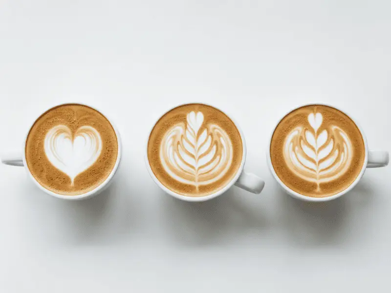 Flat White Coffee: Your Super Easy Guide to This Tasty Drink Three flat white coffees with heart, leaf, tulip latte art on thin microfoam.