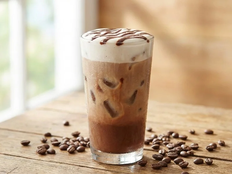 Refreshing iced hot chocolate coffee in tall glass with ice and cold foam